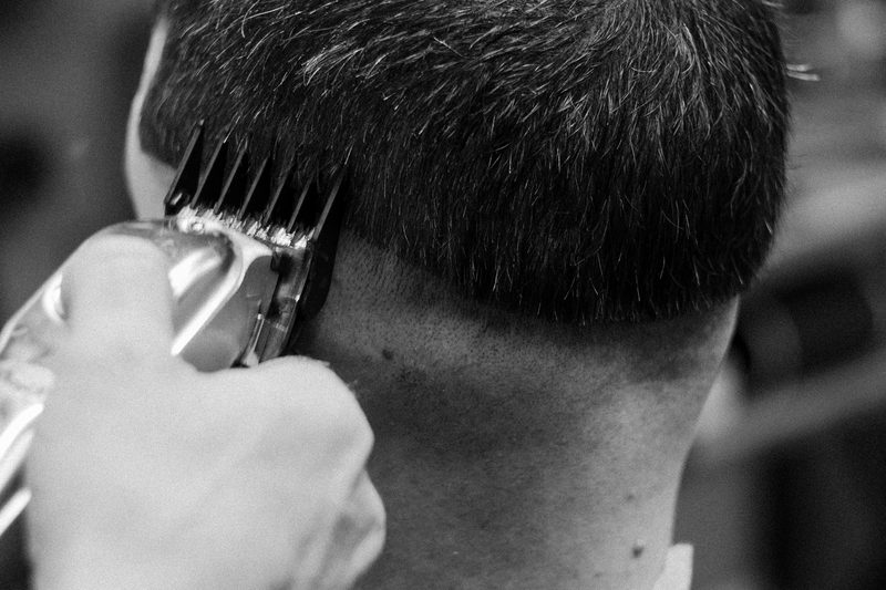Black-and-white close-up: clippers with a guard run up the back of a client's head, leaving a short, even fade at the neck.