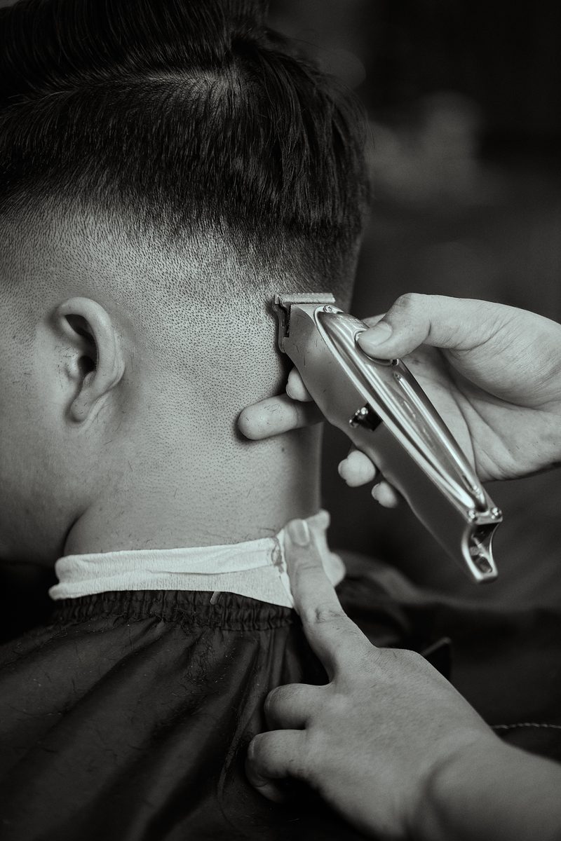 Black-and-white close-up: a trimmer edges a clean fade at the back of a client's neck.