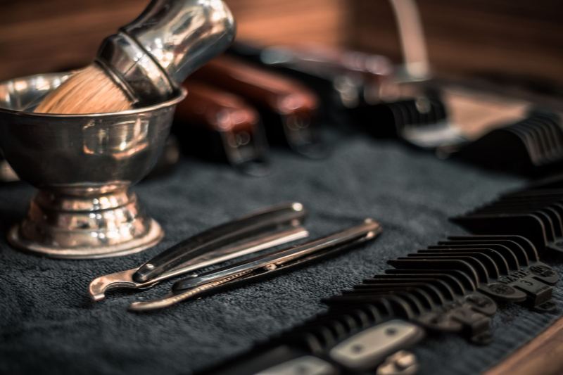 A shaving brush in a bowl beside a straight razor and clippers on dark cloth.